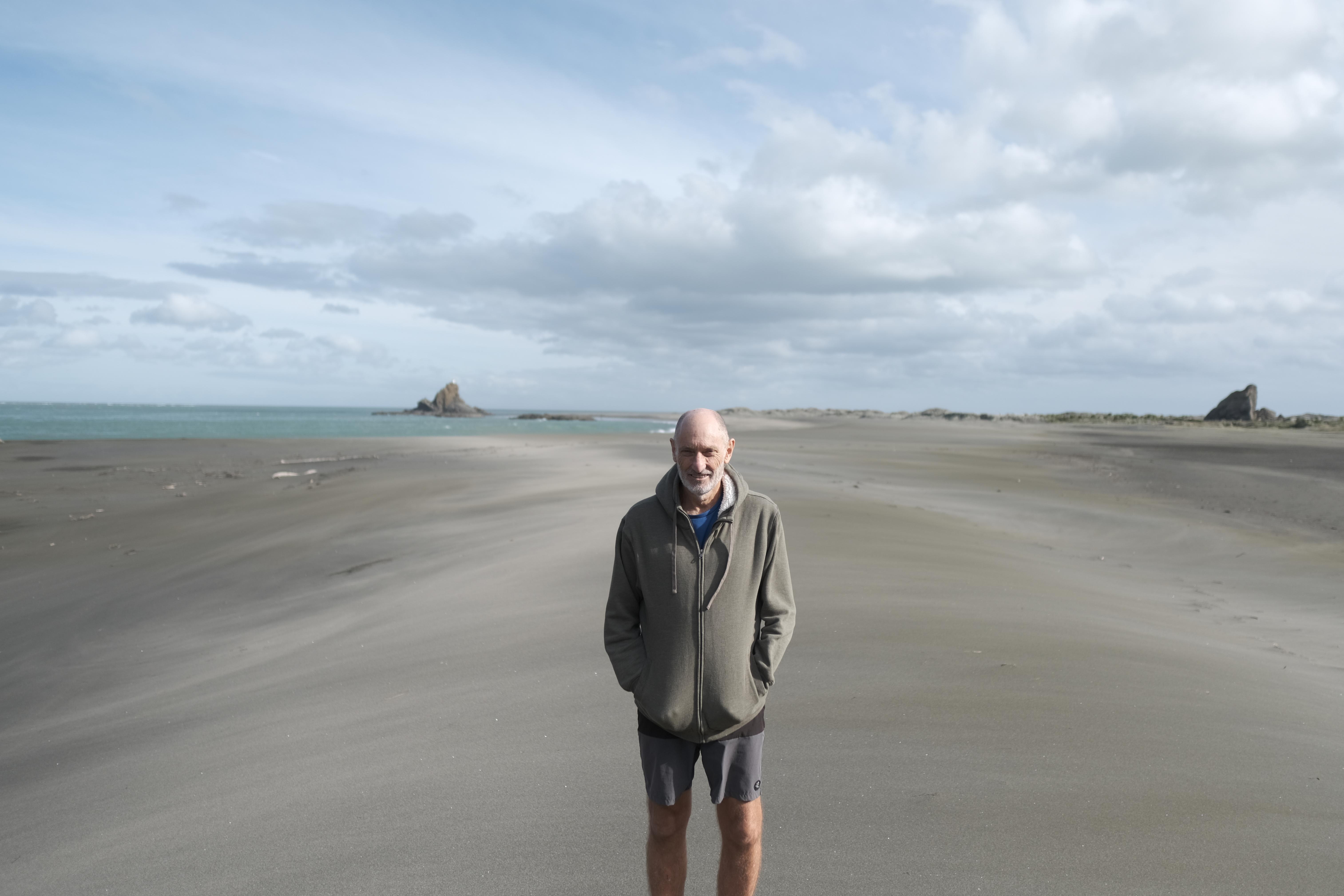 image of man standing on black sandy beach leading to the ocean